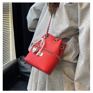 Detail of red quilted bucket bag featuring a pearl bow charm and silver chain strap