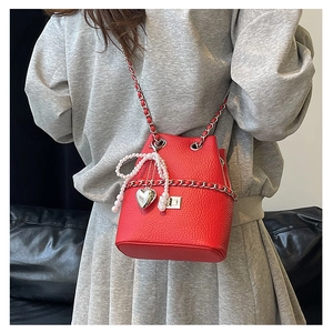 Detail of red bucket bag featuring lychee texture leather, pearl bow, and chain strap