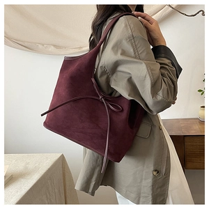 Close-up of suede texture and decorative leather bow on a burgundy shoulder tote bag
