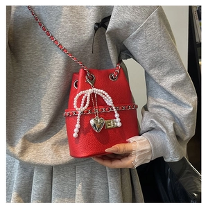 Detail of red pebble leather bucket bag with pearl bow, heart charm and silver chain strap