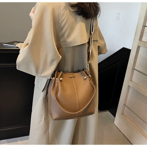Close-up of litchi grain leather bucket bag with gold hardware on a beige trench coat