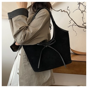 Close-up of black suede tote bag with elegant bow detail and slim leather shoulder strap
