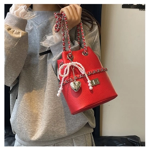 Detail of red bucket bag with lychee texture featuring pearl bow and heart pendant