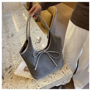 Detail of grey suede tote bag featuring a decorative bow and contrasting cream piping