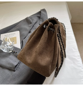 Detail of vintage brown suede bucket bag with black metal chain on grey blazer background