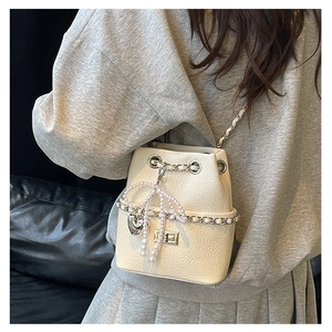 Detail of cream bucket bag with pearl bow, silver chain strap and heart charm