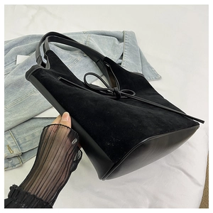 Detail of black suede tote bag with bow accent and leather handle held by hand