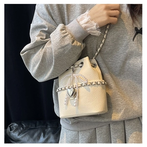 Close-up of beige quilted bucket bag with pearl bow and silver heart pendant detail