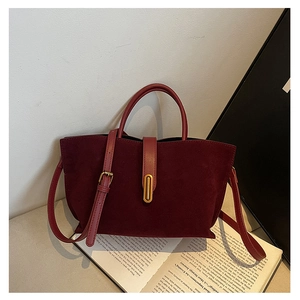 Detail of burgundy suede wing bag with golden buckle and stitching on book background