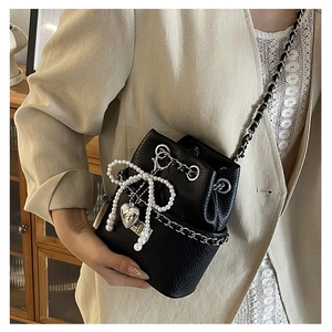 Detail of black bucket bag with pearl bow, heart pendant and silver chain strap
