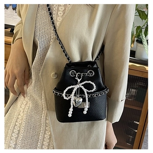 Detail of black quilted bucket bag featuring pearl bow charm and silver chain strap
