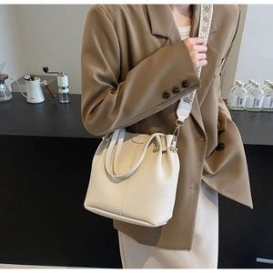 Detail of cream bucket bag with lychee texture and embroidered wide shoulder strap