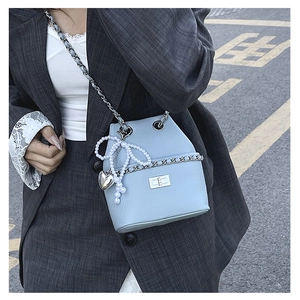 Detail of light blue leather bucket bag with silver chain strap and pearl bow charm accessory