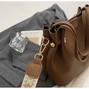 Detail of brown lychee grain leather bucket bag with jacquard strap and gold hardware
