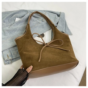 Detail shot of a dark brown suede tote bag featuring a decorative bow on light linen bedding