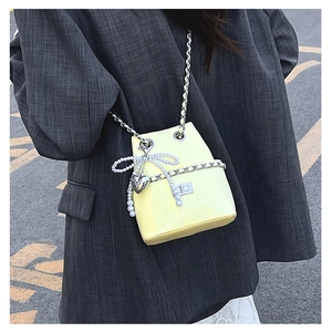 Detail of yellow bucket bag with pearl bow, heart pendant, and metal chain strap