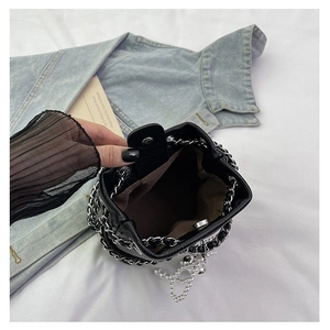 Detail of black quilted bucket bag with chain strap, pearl charm and magnetic closure
