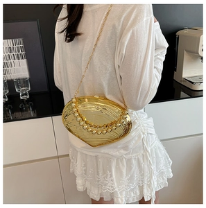 Golden shell-shaped evening bag with a metallic finish and beaded handle on a model