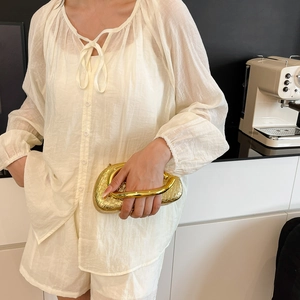 Detail of gold woven clutch bag with unique metal wrist handle held by a model