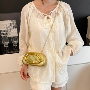 Detail of gold woven clutch featuring a large circular metal handle and slim chain strap