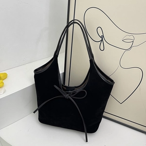 Elegant black suede tote bag with decorative bow on minimalist urban background