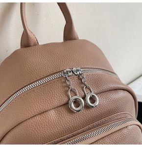Detail of camel lychee leather backpack showing dual zippers and silver ring hardware