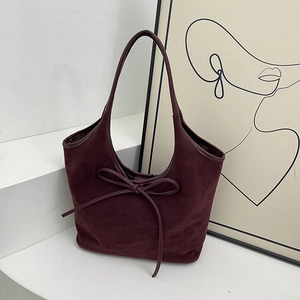 Elegant burgundy suede tote bag with large bow detail shown in a minimalist studio setting