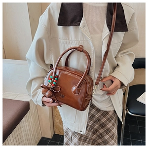 Detail of dark brown glossy leather handbag with beaded bow charm and shoulder strap