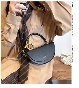 Detail of black leather saddle bag with gold metal handle worn by model in campus style
