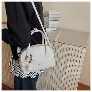 Detail of cream Boston handbag featuring adjustable strap and decorative beaded charm