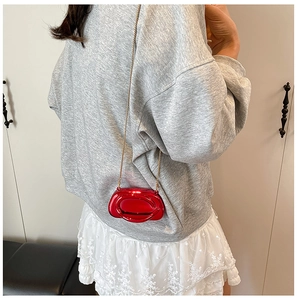 Detail of red metallic crossbody mini bag with gold chain strap on a model outfit