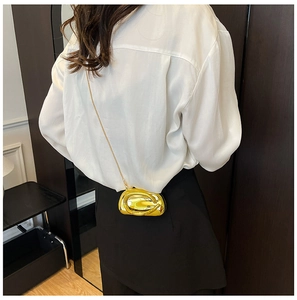 Detail of a metallic gold pebble-shaped mini bag with a fine chain on a model