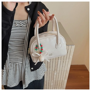 Close-up of a white mini Boston bag with a bow pearl charm and fine leather texture