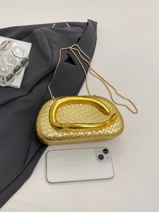 Detail of gold woven clutch bag with thick metal handle and chain against a suit backdrop