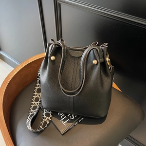 Minimalist black lychee leather bucket bag with woven wide strap and golden hardware