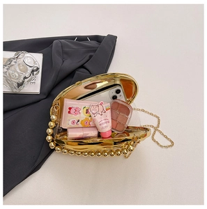 Detail of gold shell evening bag with pearl handle and metal chain on grey suit background