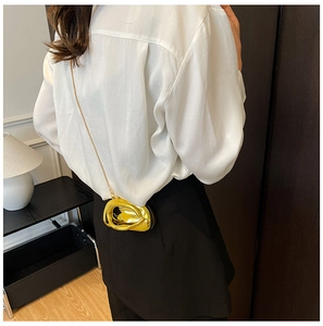 Close-up of golden irregular mini chain bag worn by a model over a white shirt