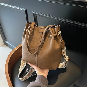Brown litchi grain bucket bag with dual handles and ethnic pattern wide strap on chair
