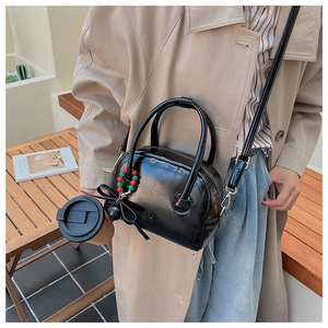 Detail of glossy black pillow bag with bead and bow charm styled with a beige coat