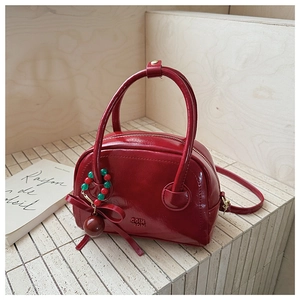 Detail of red semicircular pillow bag with bow charm and adjustable shoulder strap