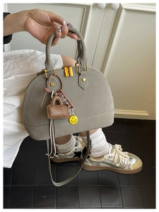Detail of grey shell handbag with gold zippers, mini charm and yellow smiley face