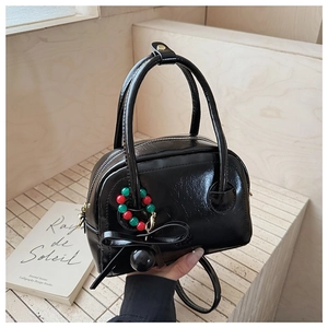 Detail of glossy black Boston handbag featuring gold hardware and beaded bow charm