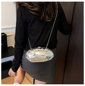 Detail view of silver shell-shaped metallic crossbody bag with sleek metal chain on model