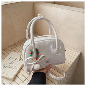 Detail of a creamy white glossy bag with an oversized bow and colorful beaded charm