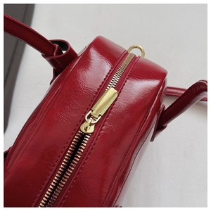 Close-up of a deep red pillow bag featuring shiny oil wax leather and gold metal zipper detail