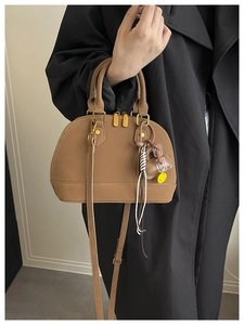 Detail of a brown shell handbag with gold zippers and a stylish emoji charm accessory