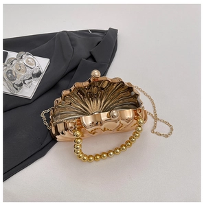 Détail d'un sac de soirée doré en forme de coquillage avec poignée perlée et chaîne