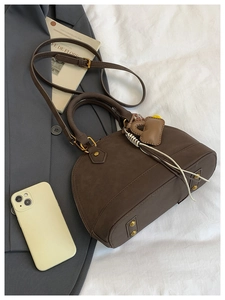 Close-up of brown shell bag showing matte leather texture, heart charm and metal feet