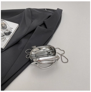 Macro detail of silver fluid-metal chain bag showing mirror texture on a stylish blazer