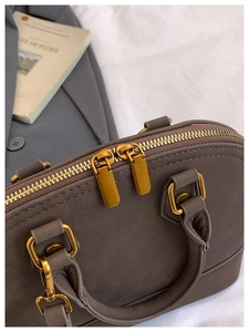 Detail view of smooth dark brown leather shell bag with gold zippers and hardware